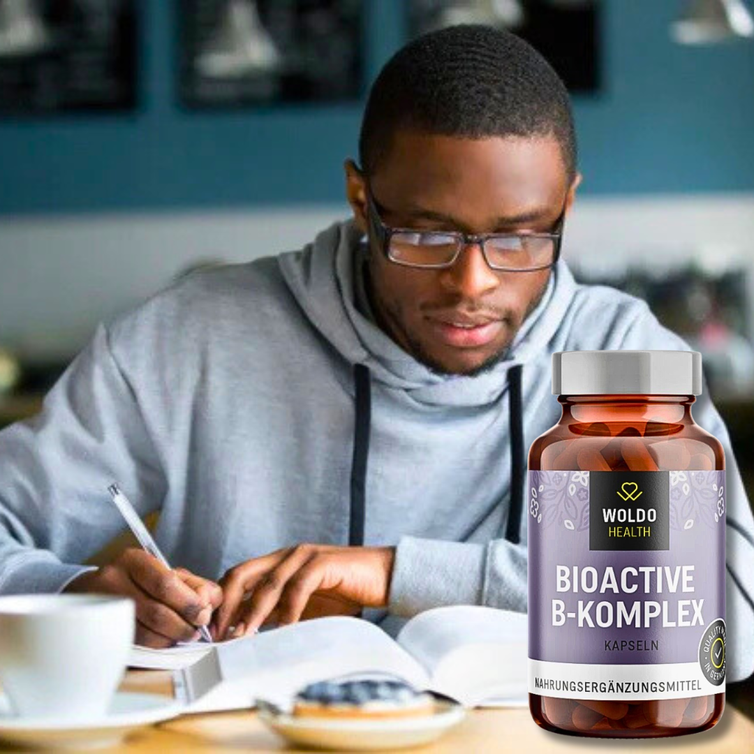 “Man studying at a desk with an open notebook; foreground shows WoldoHealth Bioactive B-Complex capsules bottle.”